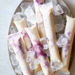 Blackberry pineapple coconut ice pops on a plate with ice.