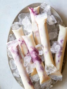Blackberry pineapple coconut ice pops on a plate with ice.