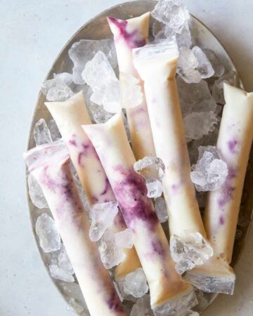 Blackberry pineapple coconut ice pops on a plate with ice.