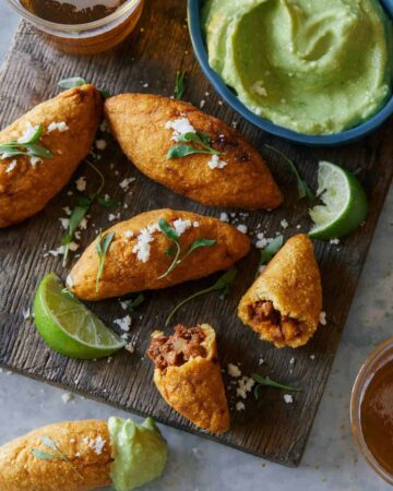 A close up of chorizo molotes with lime wedges and sauce on the side.