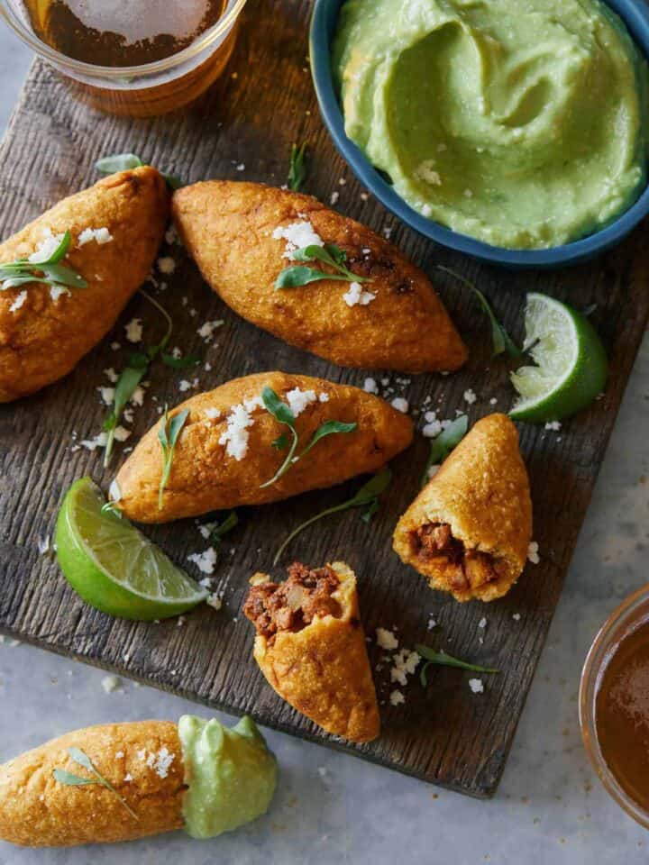 A close up of chorizo molotes with lime wedges and sauce on the side.