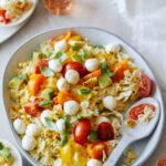 A plate of loaded pasta salad with a spoon.