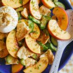 A close up of peach panzanella salad with a spoon.