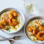 Bowls of fried shrimp and grits with forks and a drink.