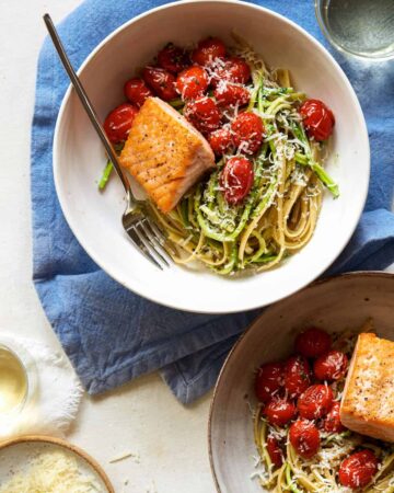 Seared salmon over 50/50 spaghetti with arugula and walnut pesto with a fork.