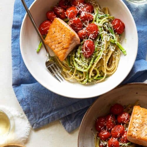 Seared salmon over 50/50 spaghetti with arugula and walnut pesto with a fork.