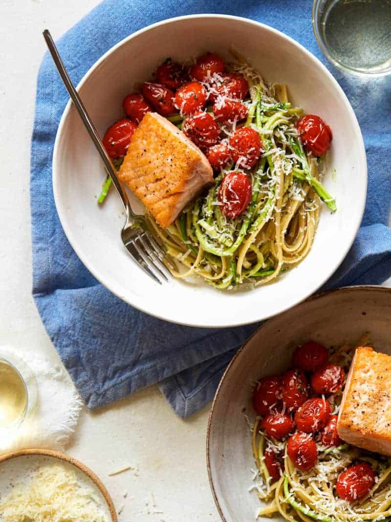 Seared salmon over 50/50 spaghetti with arugula and walnut pesto with a fork.