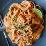 A close up of red curry noodles with a lime wedge and a fork.