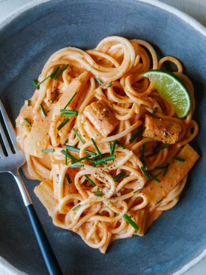 A close up of red curry noodles with a lime wedge and a fork.