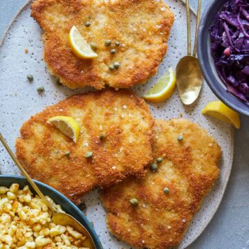 Schnitzel with buttered spaetzle with sweet and sour cabbage, lemon wedges and spoons.