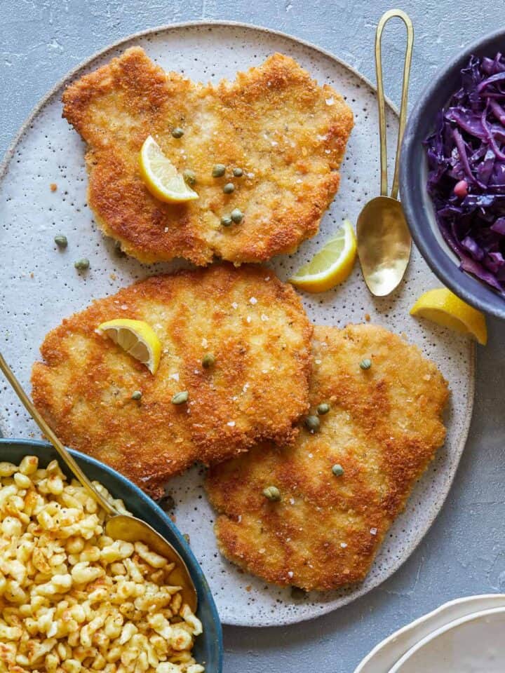 Schnitzel with buttered spaetzle with sweet and sour cabbage, lemon wedges and spoons.