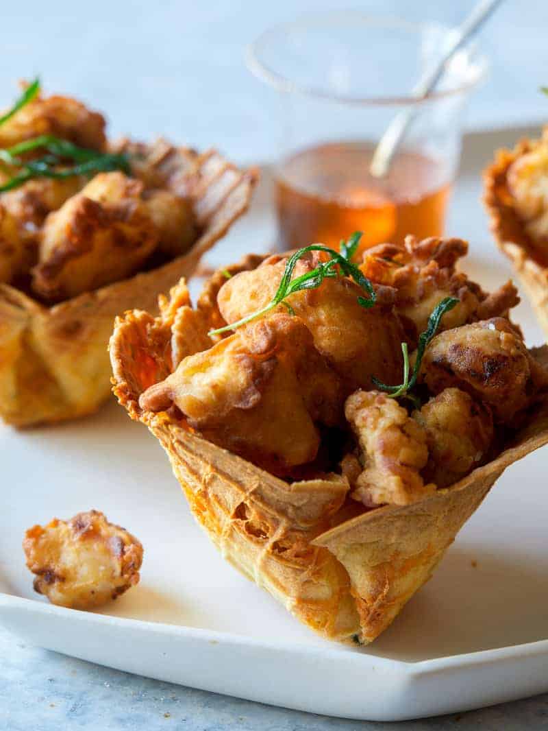 A close up of popcorn chicken in a cheesy waffle cone.