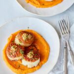 A plate of seared scallops over roasted sweet potato pureee with forks.