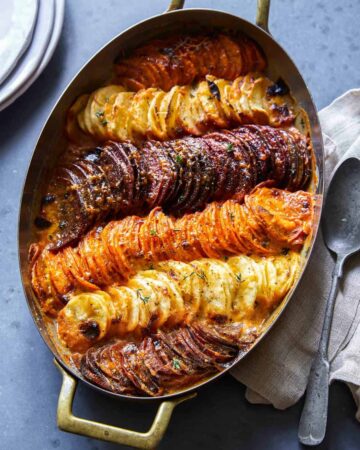 An oval baking dish of cheesy root vegetable gratin with a spoon.