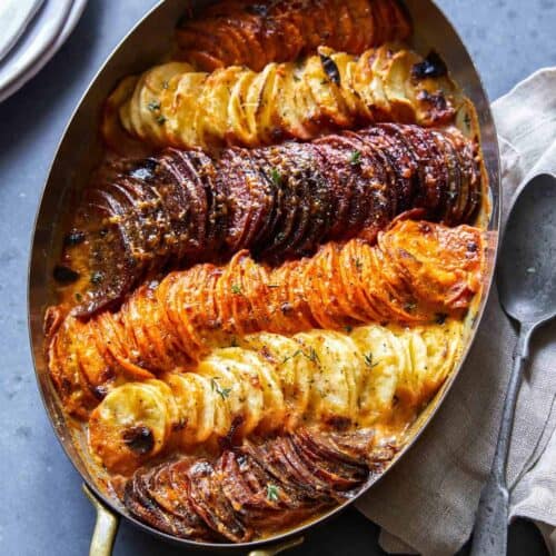 An oval baking dish of cheesy root vegetable gratin with a spoon.