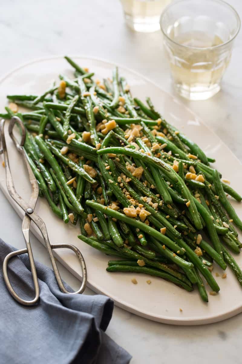 A platter of lightly roasted green beans with serving tongs.