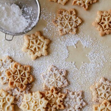 Gingerbread snowflake cookies being dusted with sugar.
