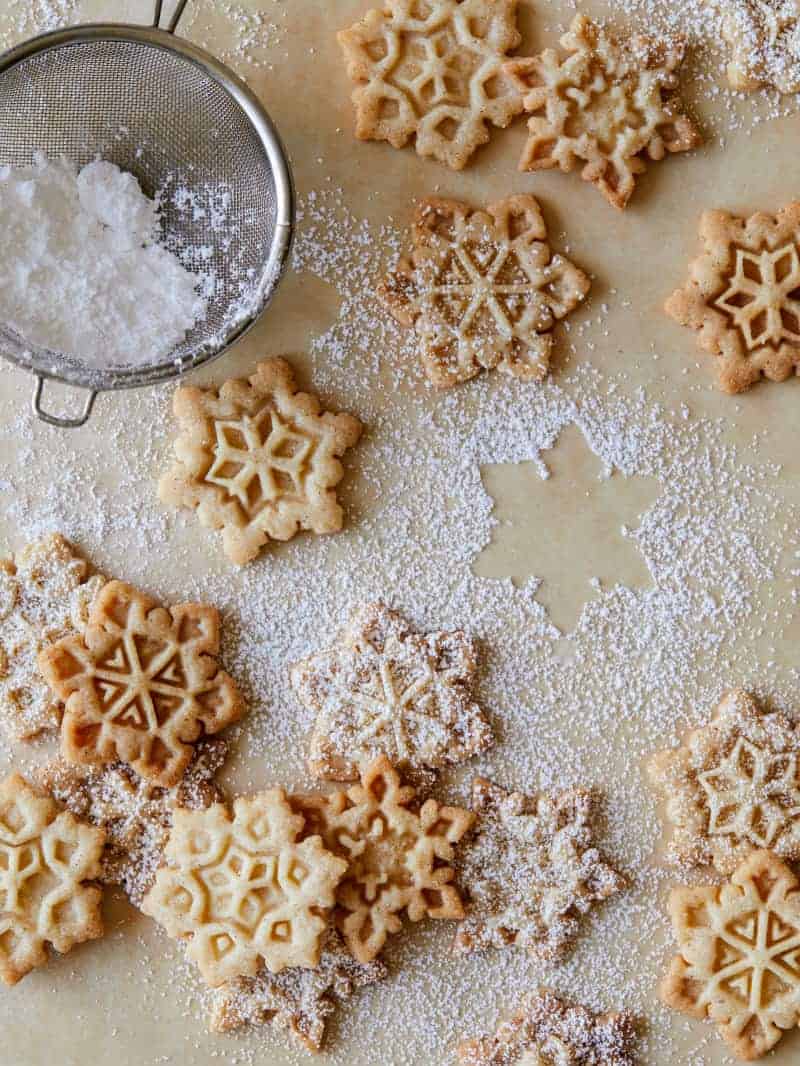 Gingerbread snowflake cookies being dusted with powdered sugar through a sieve.