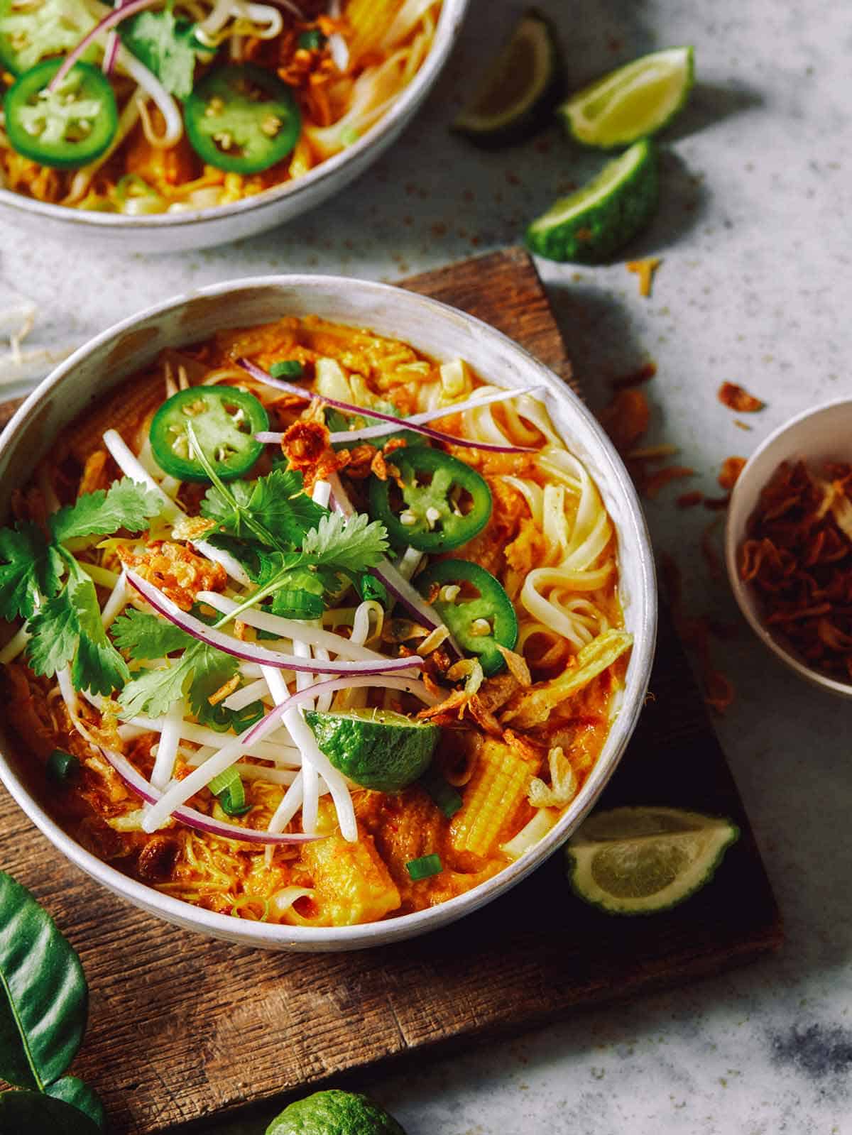 Spicy chicken laksa in two bowls with onions on the side.