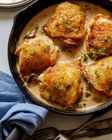 A close up of crispy chicken thighs with a creamy mushroom sauce in a skillet.