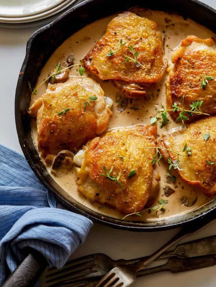 A close up of crispy chicken thighs with a creamy mushroom sauce in a skillet.