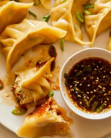 A close up of ginger chicken pot stickers with green onions and sauce.