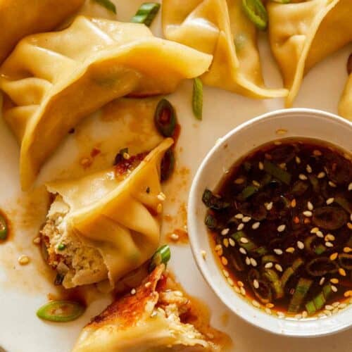 A close up of ginger chicken pot stickers with green onions and sauce.