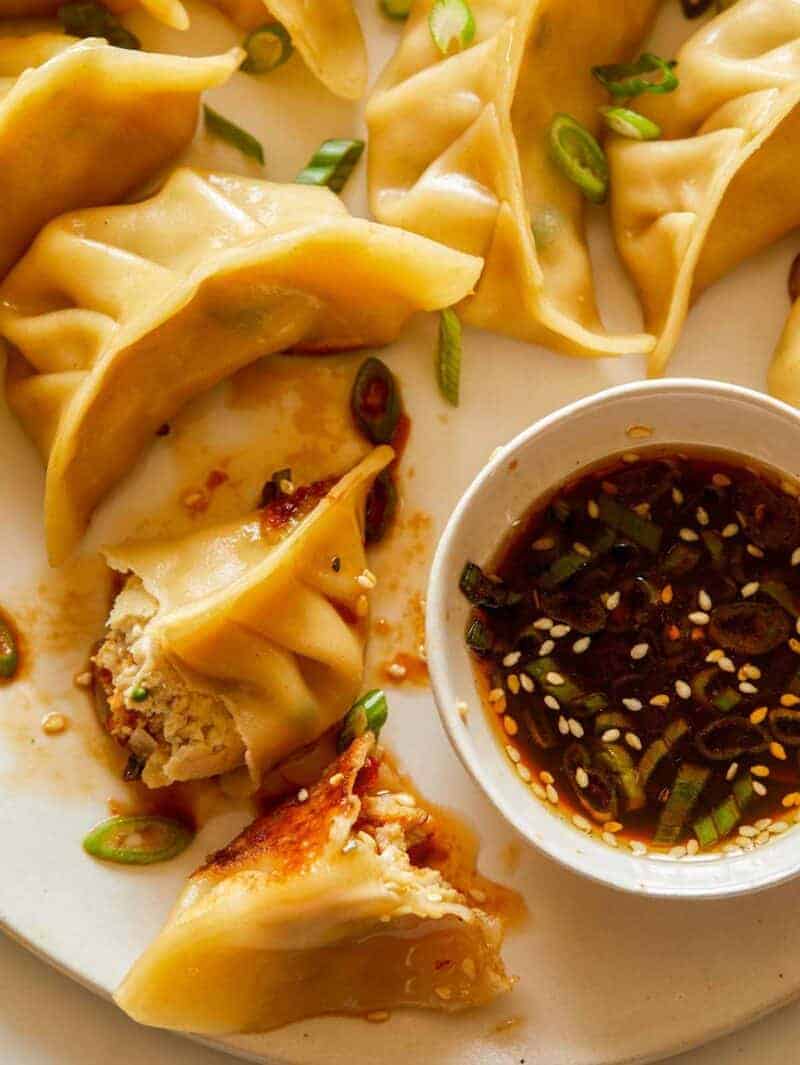 A close up of ginger chicken pot stickers with green onions and sauce.