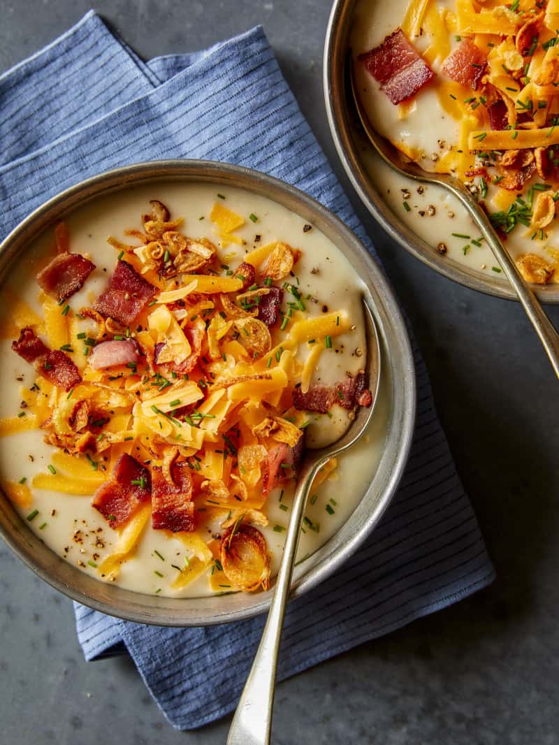 A close up of bowls of loaded baked potato soup with a blue napkin and spoons.