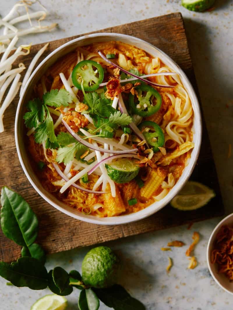 Spicy chicken laksa in a bowl garnished with jalapeños, red onion, and cilantro.