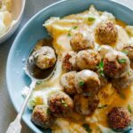 Vegan swedish meatballs over mashed potatoes and gravy with a spoon.
