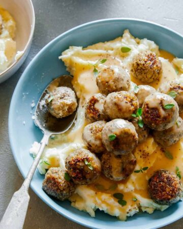 Vegan swedish meatballs over mashed potatoes and gravy with a spoon.