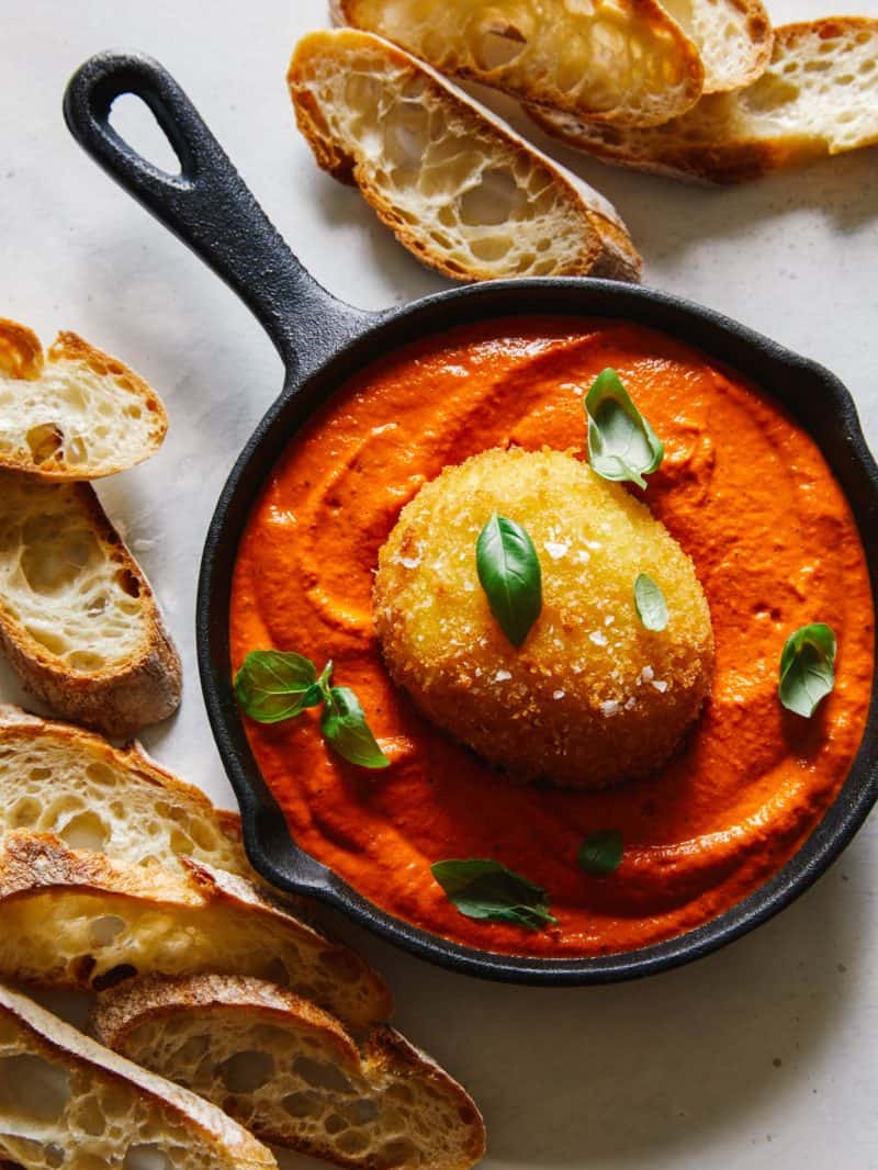 Fried burrata over romesco sauce in a skillet with bread.