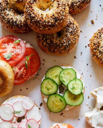 Everything bagels, some sliced and topped with cream cheese and veggies.