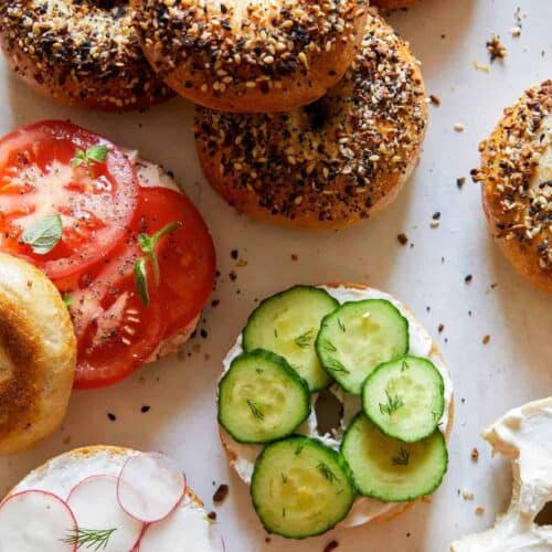 Everything bagels, some sliced and topped with cream cheese and veggies.