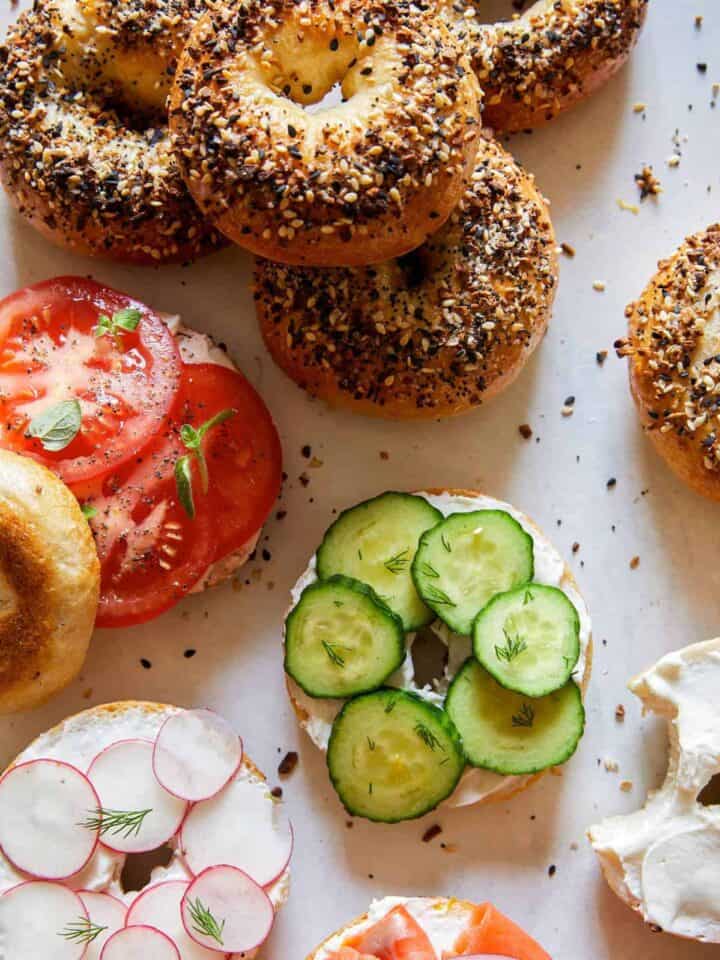Everything bagels, some sliced and topped with cream cheese and veggies.