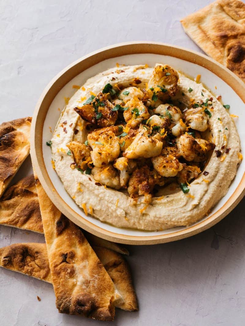 Spicy roasted cauliflower over hummus in a bowl with pita chips.