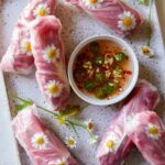 Fresh shiitake spring rolls with edible flowers and sauce on the side.