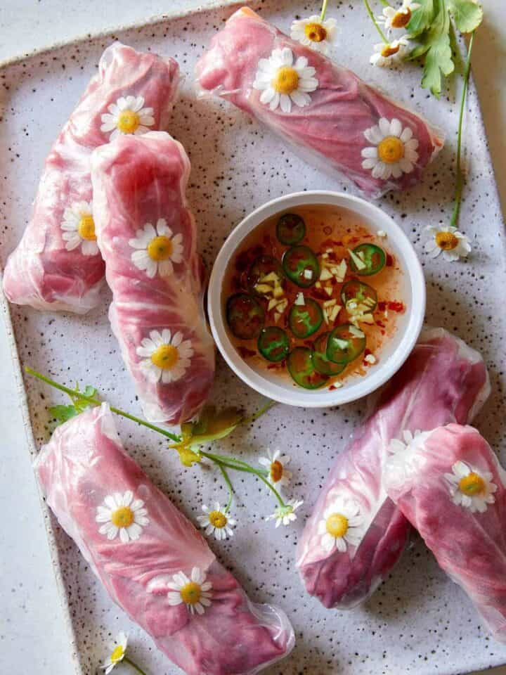 Fresh shiitake spring rolls with edible flowers and sauce on the side.