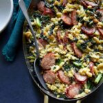 A close up of sausage kale and spaetzle pesto bake in a pan with a spoon.