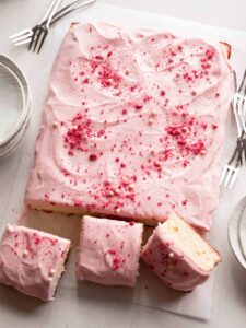 A sliced vanilla bean sheet cake with strawberry frosting and forks.