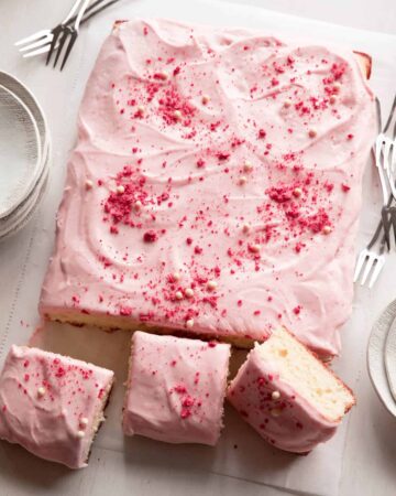 A sliced vanilla bean sheet cake with strawberry frosting and forks.
