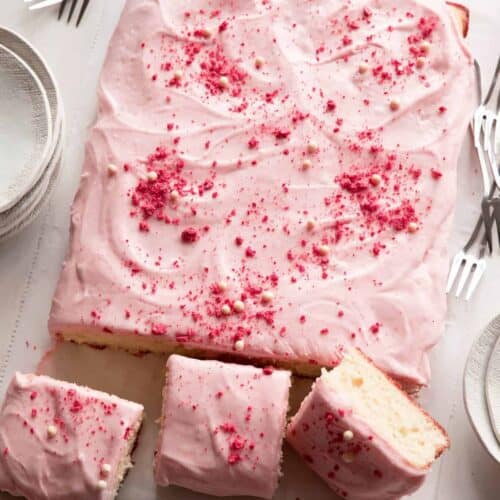 A sliced vanilla bean sheet cake with strawberry frosting and forks.