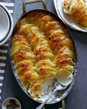 Cheesy garlic potato gratin in an oval baking dish with a scoop taken out with a spoon.