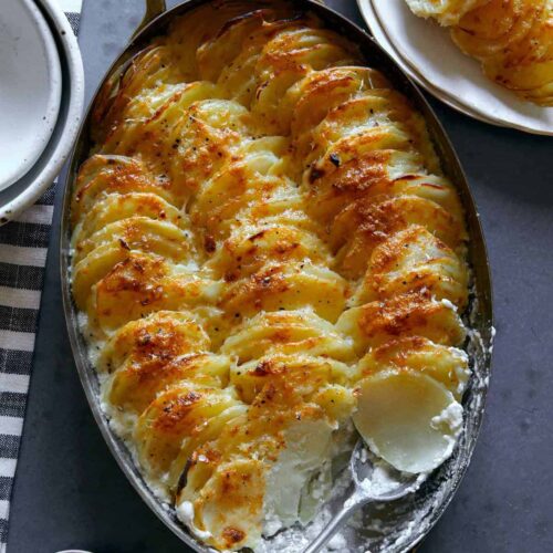 Cheesy garlic potato gratin in an oval baking dish with a scoop taken out with a spoon.