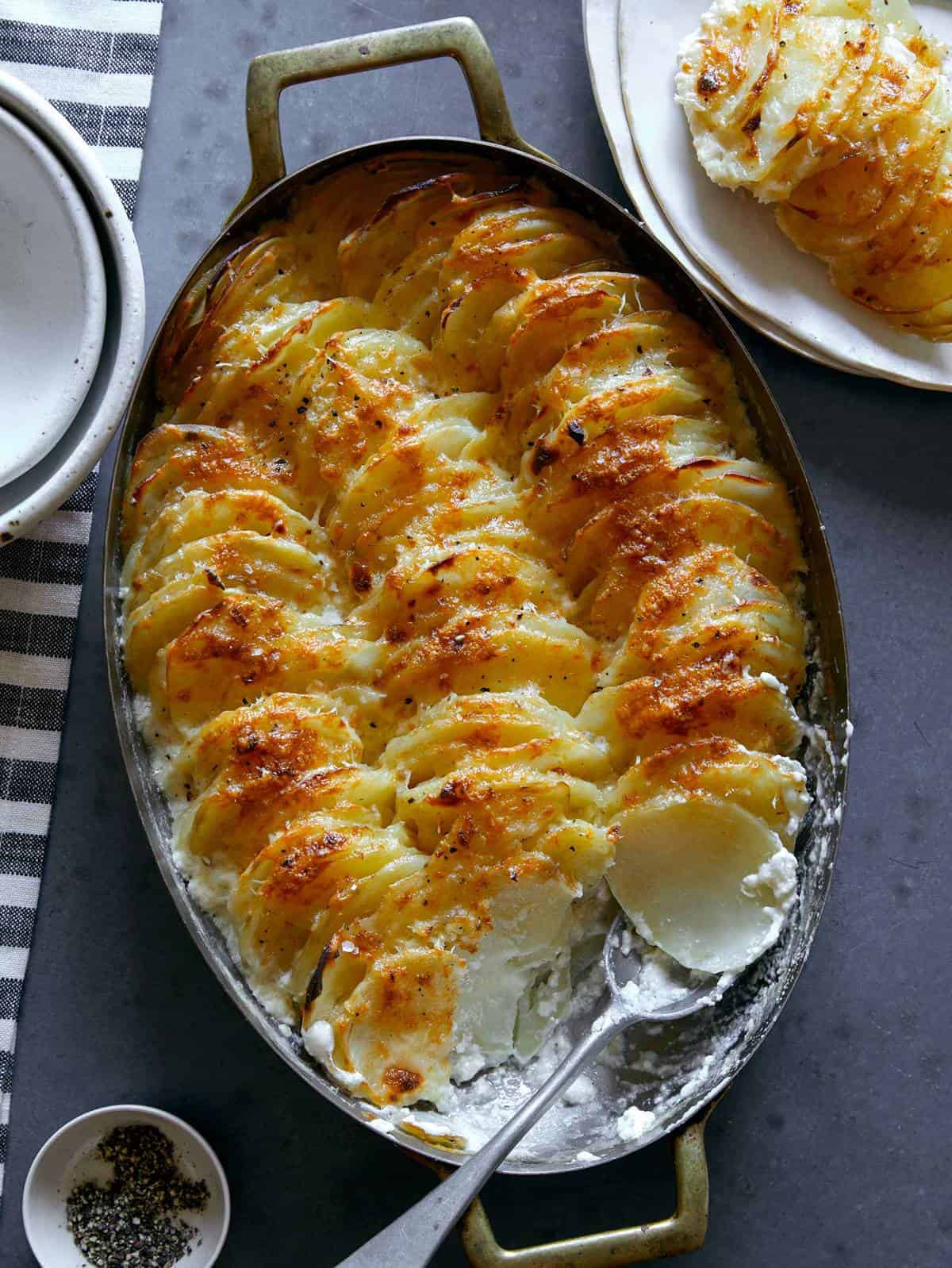 Cheesy garlic potato gratin in an oval baking dish with a scoop taken out with a spoon.