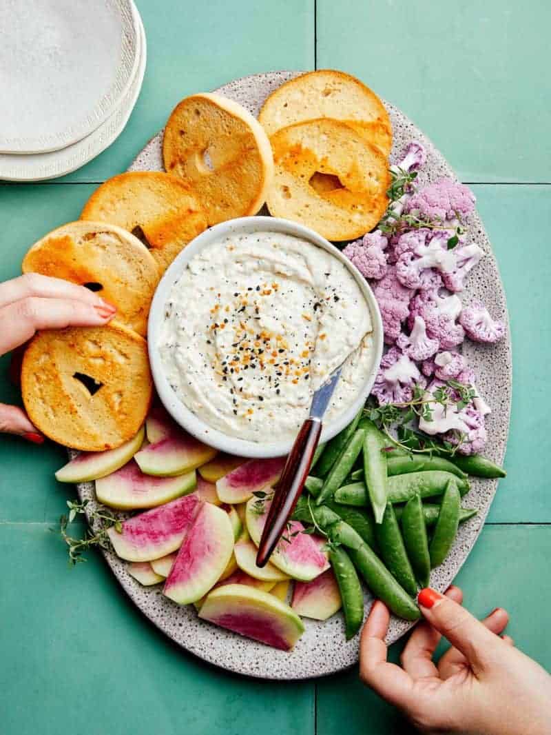 A bowl of everything seasoning dip on a platter of bagels and veggies.