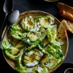 Grilled avocado and gem salad topped with herb yogurt dressing with spoons.