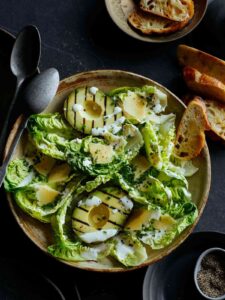 Grilled avocado and gem salad topped with herb yogurt dressing with spoons.