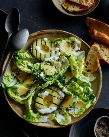 Grilled avocado and gem salad topped with herb yogurt dressing with spoons.